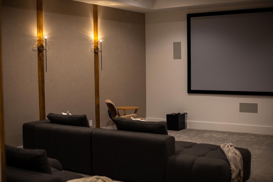 home theater room with subwoofer on the floor and in-wall speakers flanking the large projection screen.