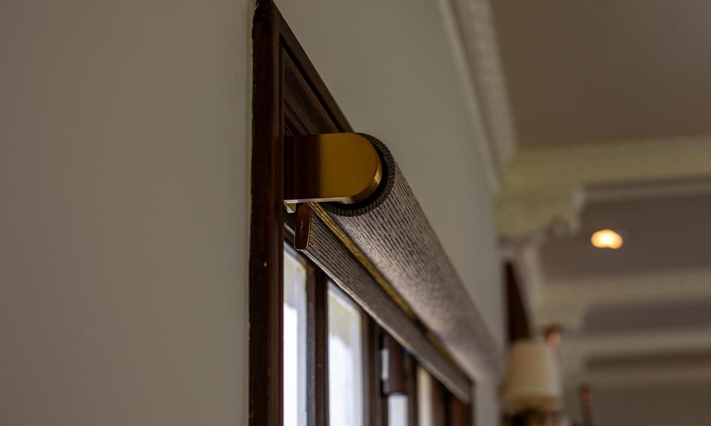 Angled view of a single roller shade with gold hardware against a white interior wall