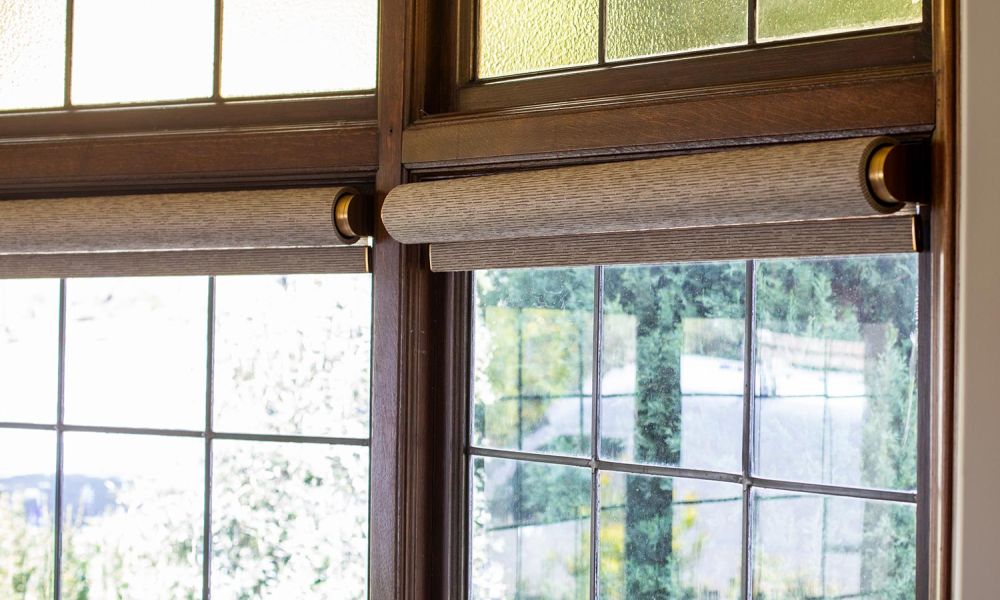 Dual roller shades installed on stained wood frame windows with patterned glass above