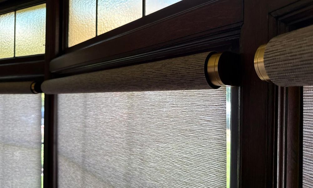 Close-up of textured roller shades with brass hardware mounted on dark wood window frames