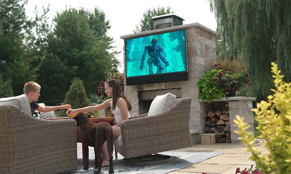 two children and a dog sit outside in a TV viewing area